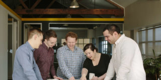 A group of people from the Arlo team stand around a table reviewing a document.