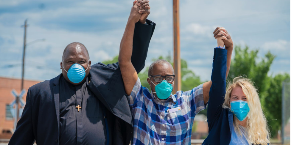 Three people with their hands linked and raised They are celebrating the release from prison of the man in the middle who was wrongfully imprisoned for more than 40 years