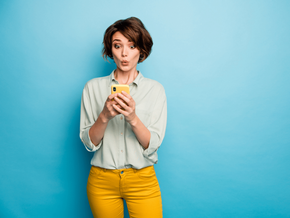 National Telephone Day: 10 mind-blowing facts about phones | #customersupport - purshoLOGY Woman in light blue top and orange pants on a blue background looking pleasantly surprised at her smartphone