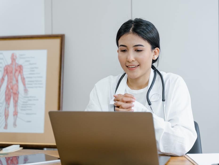 A healthcare provider sits at her desk in front of a laptop for a telehealth appointment