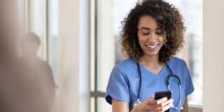 Attractive young female nurse or doctor checks messages on smartphone as she walks in a hospital hallway.