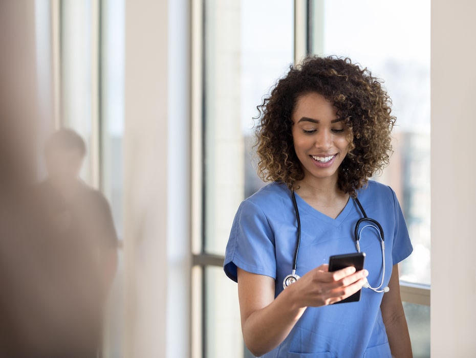 Attractive young female nurse or doctor checks messages on smartphone as she walks in a hospital hallway