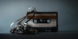Retro audio cassette with tape out placed on gray surface and illuminated by light in studio