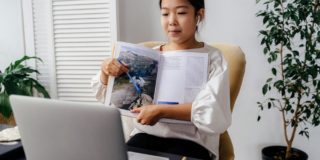Girl Holding Book in Front of Silver Laptop