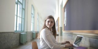 Female student typing on laptop in university hallway