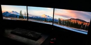 Contemporary computer with picturesque nature photos on monitors near keyboard and mouse in dark room