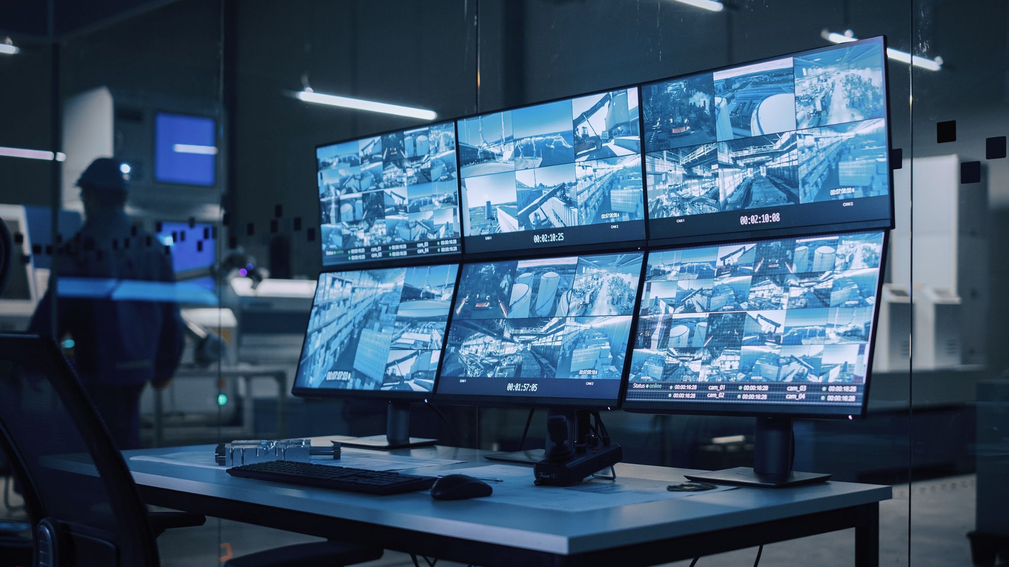 image - purshoLOGY Security operations center with a curved video wall showing multiple CCTV feeds and a technician in the background wearing a hard hat.