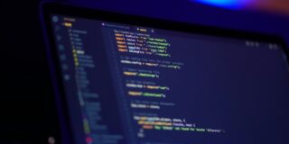 Close-up of a laptop screen displaying colorful code in a dim, blue-lit room.