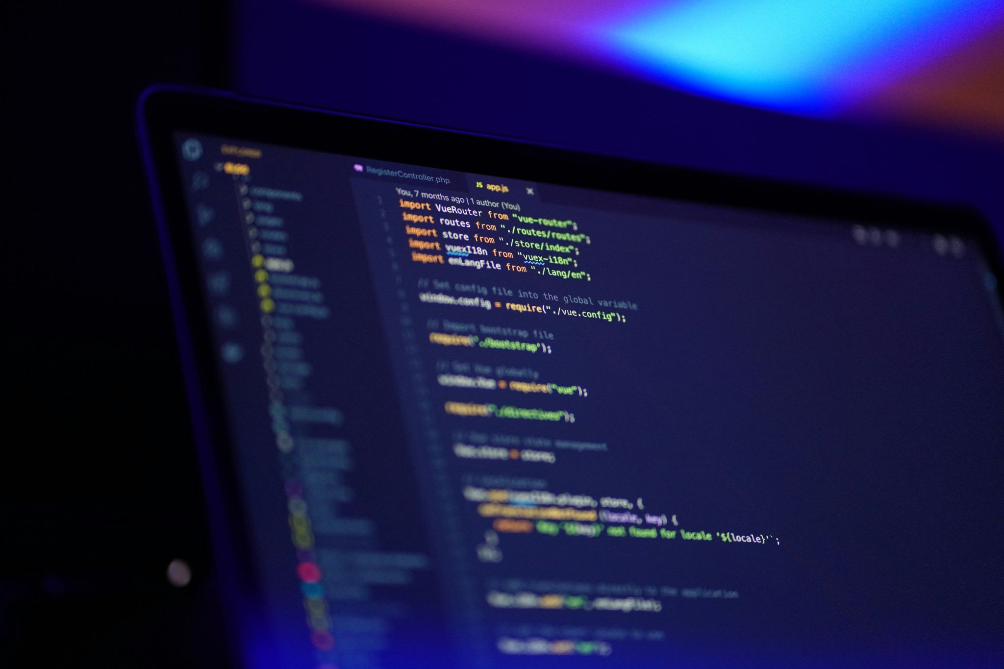 Close-up of a laptop screen displaying colorful code in a dim, blue-lit room.