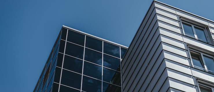 Angled view of a modern glass office building with metal siding against a clear blue sky.