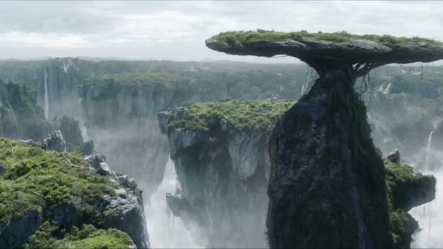 A dramatic landscape showing a tall rock pillar with a flat, grassy top, forming a mushroom-like formation over a misty canyon.