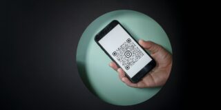 Hand holding a smartphone displaying a QR code on the screen against a green circular backdrop.