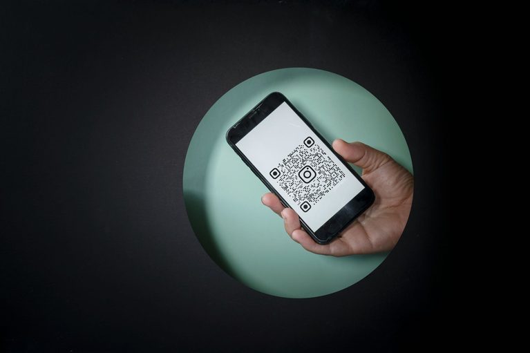 Hand holding a smartphone displaying a QR code on the screen against a green circular backdrop.
