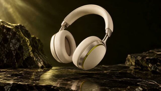White over-ear headphones resting on a dark, reflective marble surface with rocky background.